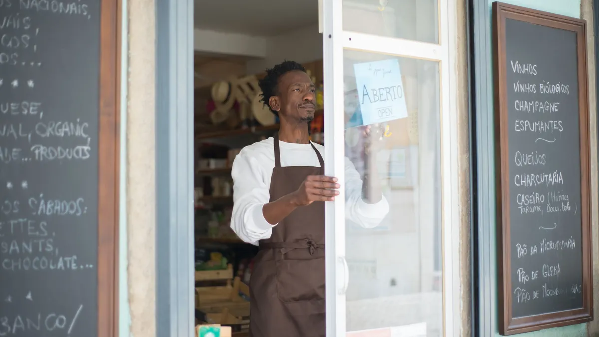 Commerçant en tablier ouvrant la porte de son commerce de proximité